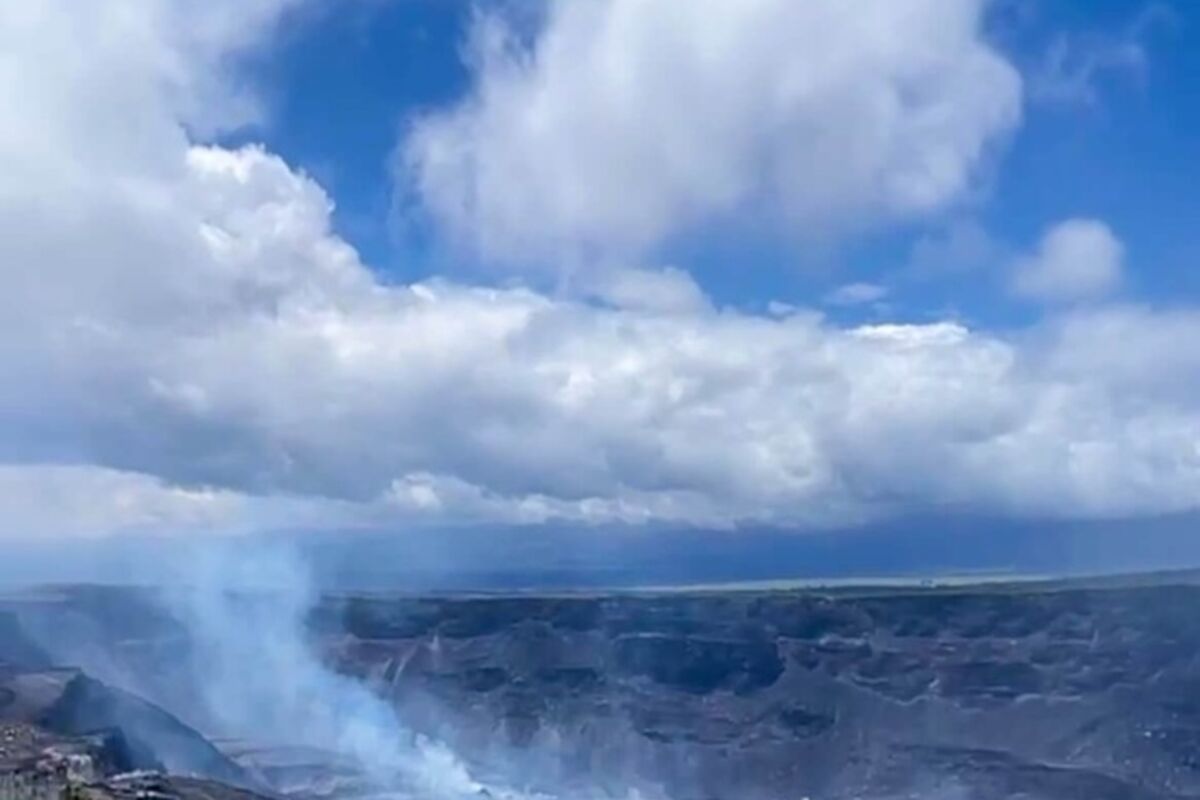 An active volcano in the distance on the edge of a cliff during the day.