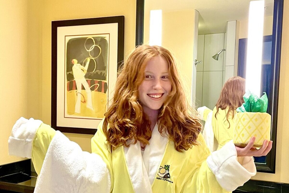 Girl in yellow bathrobe in bathroom holding towel and T.P. wrapped like a pineapple.