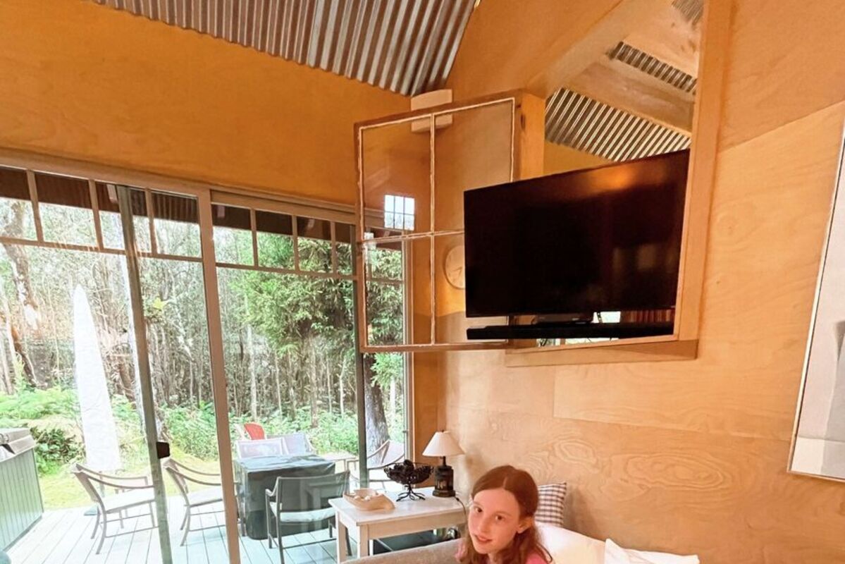 A girl enjoying a Hawaiian bungalow sitting on a bed with rainforest outside.