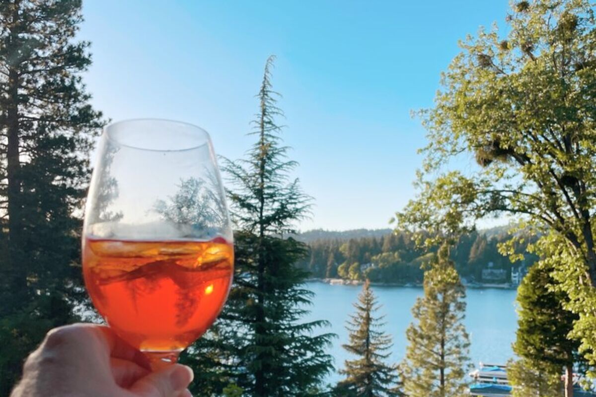 Holding an aperol spritz on balcony overlooking Lake Arrowhead.