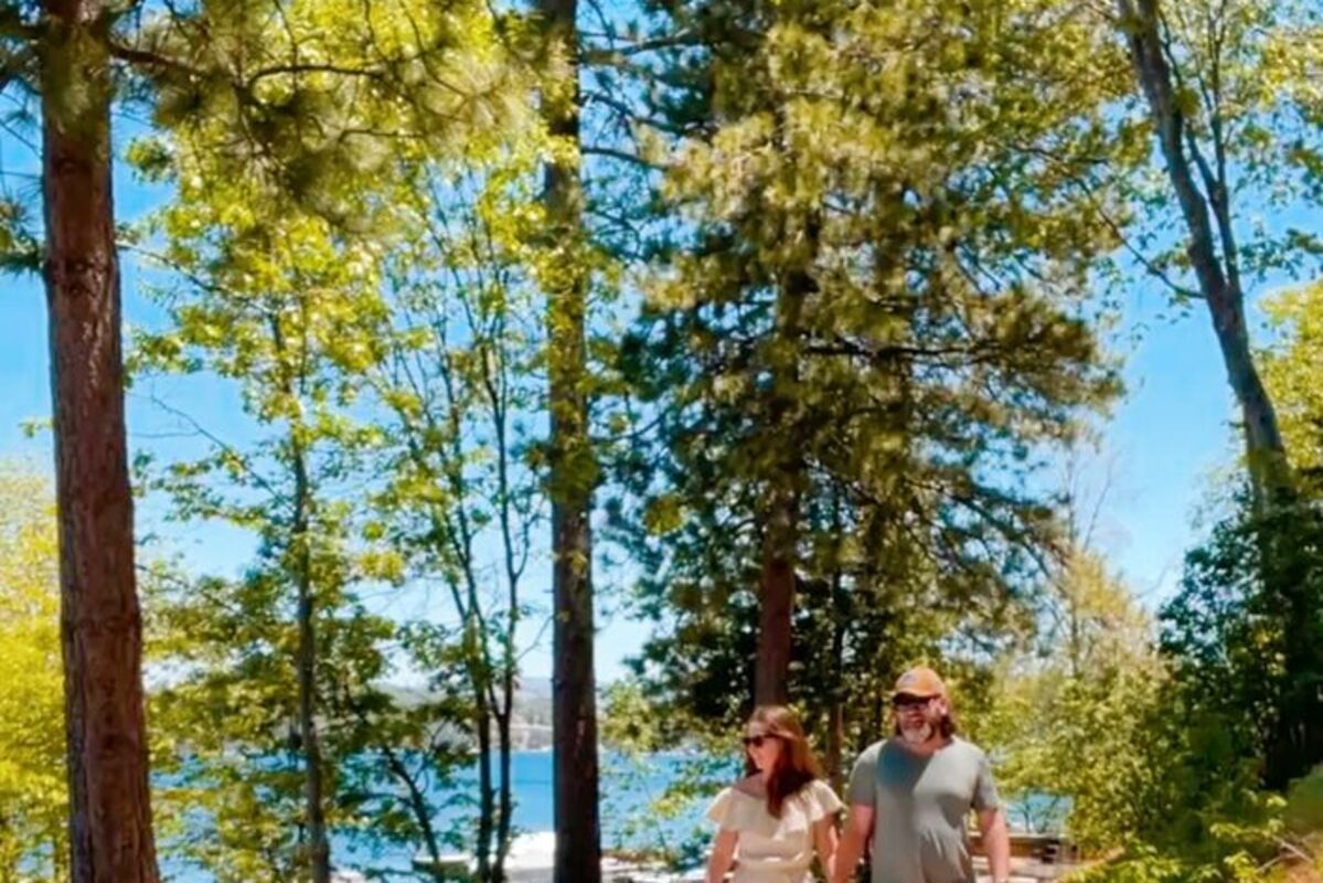 Couple walking with dog. Trees and lake in background.