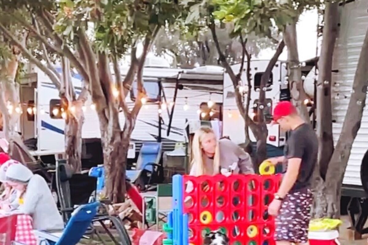 Family playing a giant Connect Four game on a field with people sitting nearby.